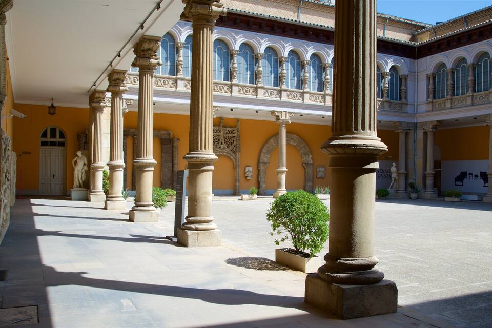 Um pátio com colunas clássicas, arcos e uma estátua.
