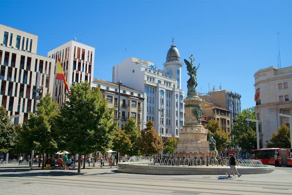 Une place de ville avec une fontaine, des bâtiments et une statue.