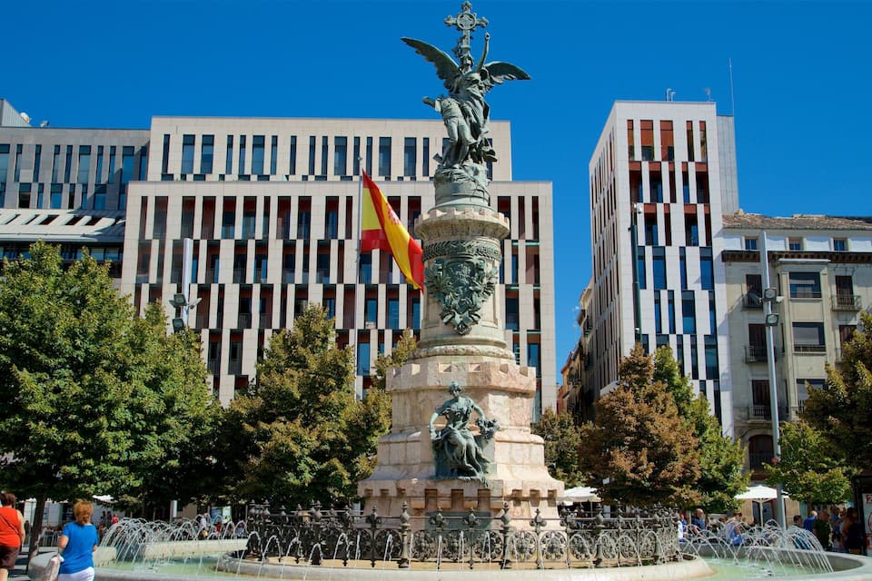 Uma fonte com uma estátua, rodeada por árvores e edifícios.