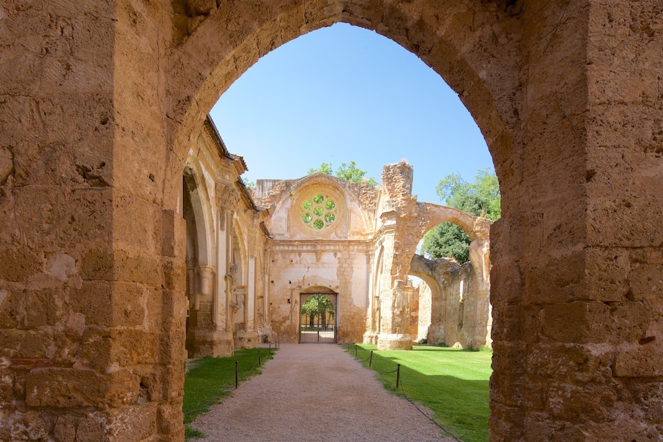 Un arc en pierre datant de l’Antiquité mène à un bâtiment historique dont la façade est ornée d’un emblème vert.