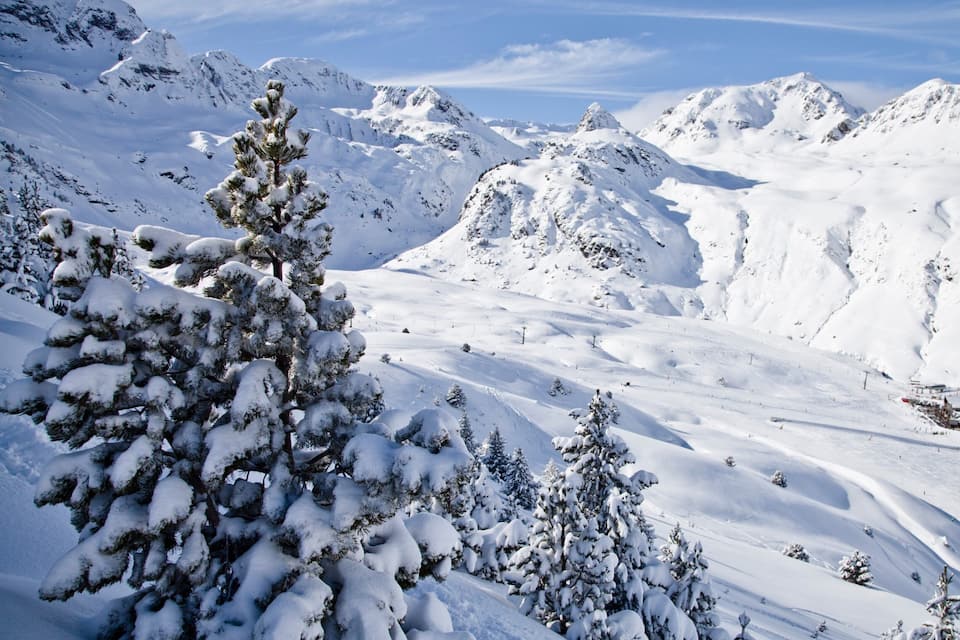 A snow-covered mountain landscape with pine trees and a ski resort.