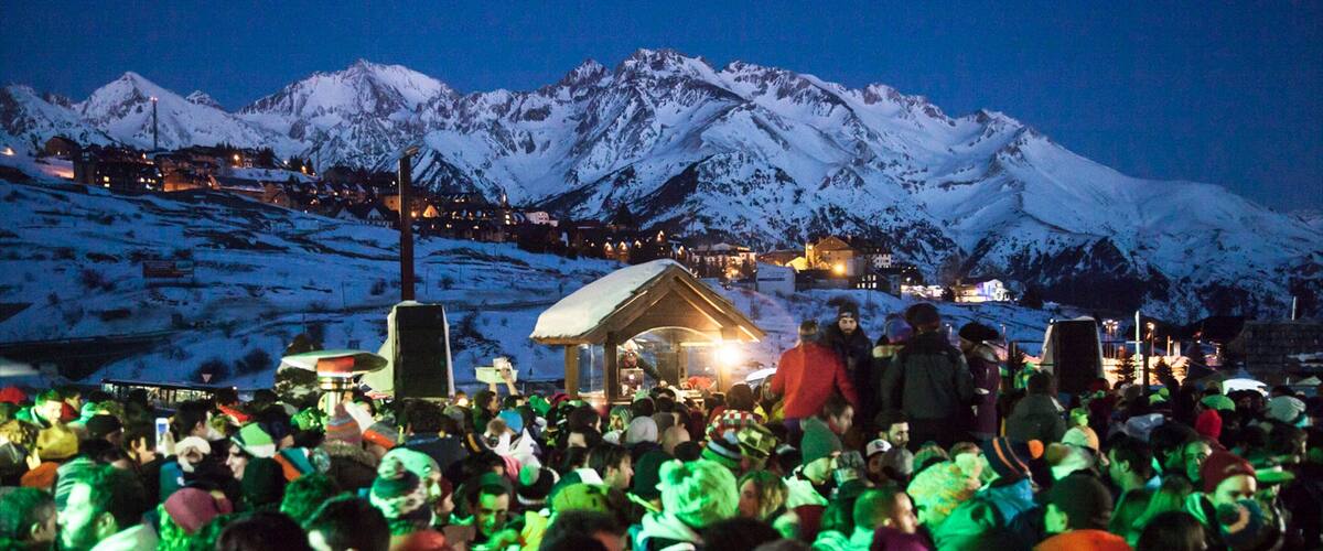 A crowd gathered in a snowy mountainous area with a stage and buildings in the background.