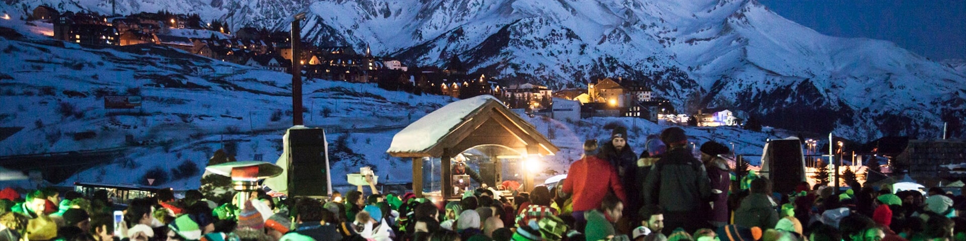 A crowd gathered in a snowy mountainous area with a stage and buildings in the background.