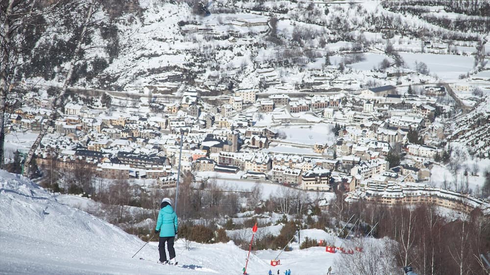 Un village enneigé, avec des maisons et une personne qui fait du ski sur une pente.