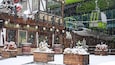 A snowy outdoor scene with a building that has signs in a foreign language, wooden planters with plants, and a green vehicle in the background.