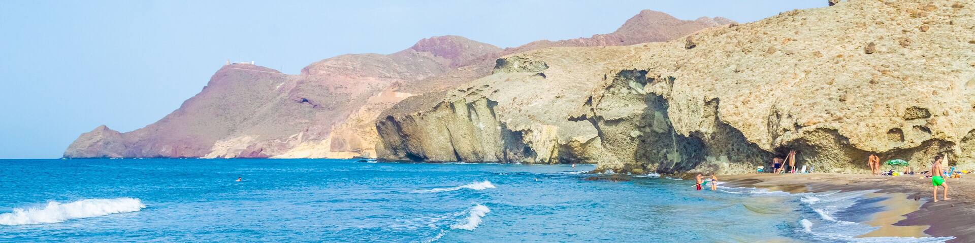 A beach with clear blue waters, rocky cliffs, and people enjoying the seaside.