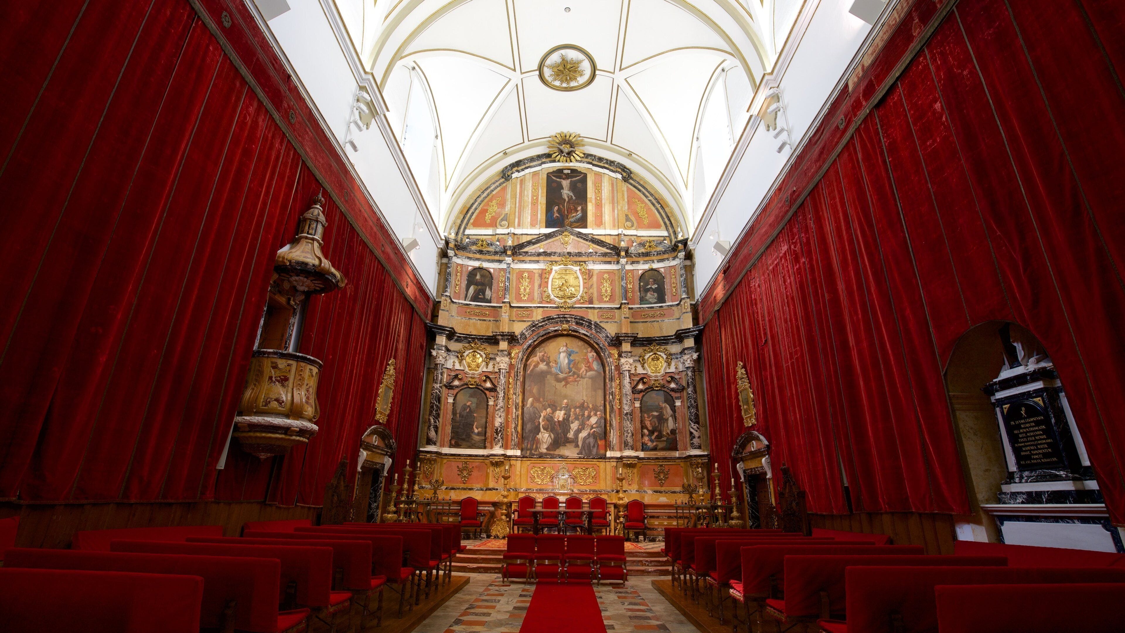 En utsmyckad kyrkinteriör med röda sammetsgardiner, ett centralt placerat altare och en stor väggmålning som föreställer en religiös scen.
