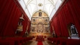 L’intérieur d’une église richement décorée, avec des rideaux de velours rouge, un autel central et une grande fresque représentant une scène religieuse.
