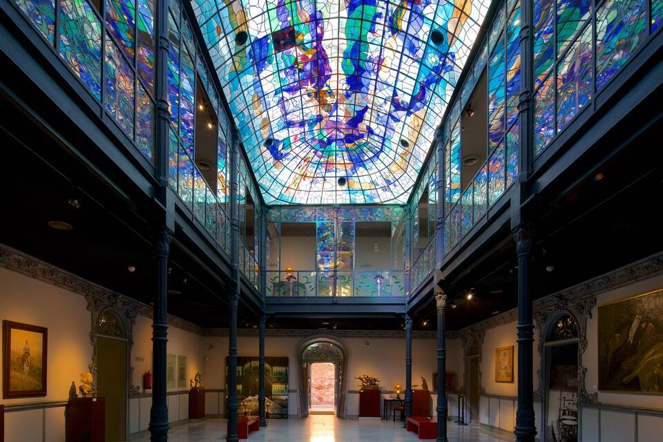A grand hall with a stunning stained glass ceiling, ornate columns, and classical paintings.