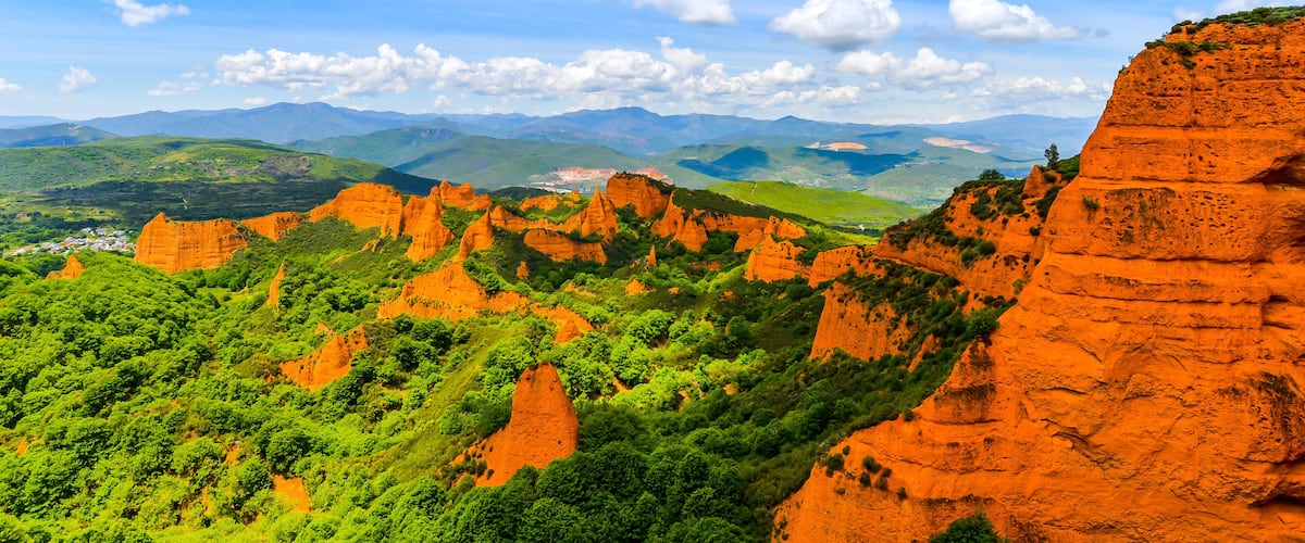 A mountainous landscape with red rock formations and green vegetation under a blue sky.
