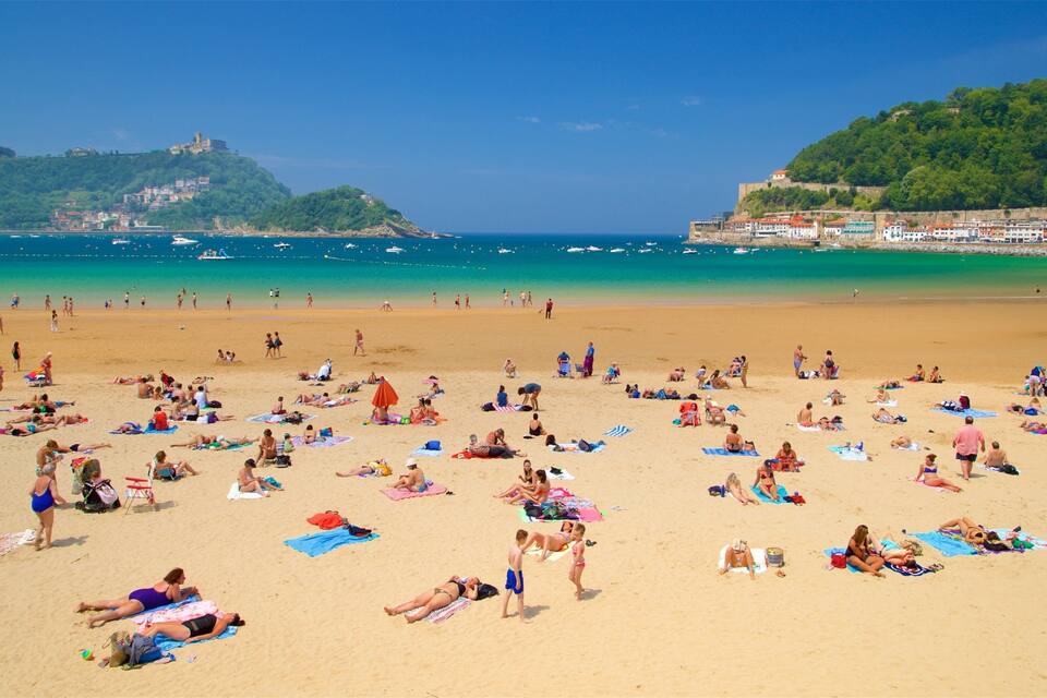 A crowded beach with people sunbathing and swimming.