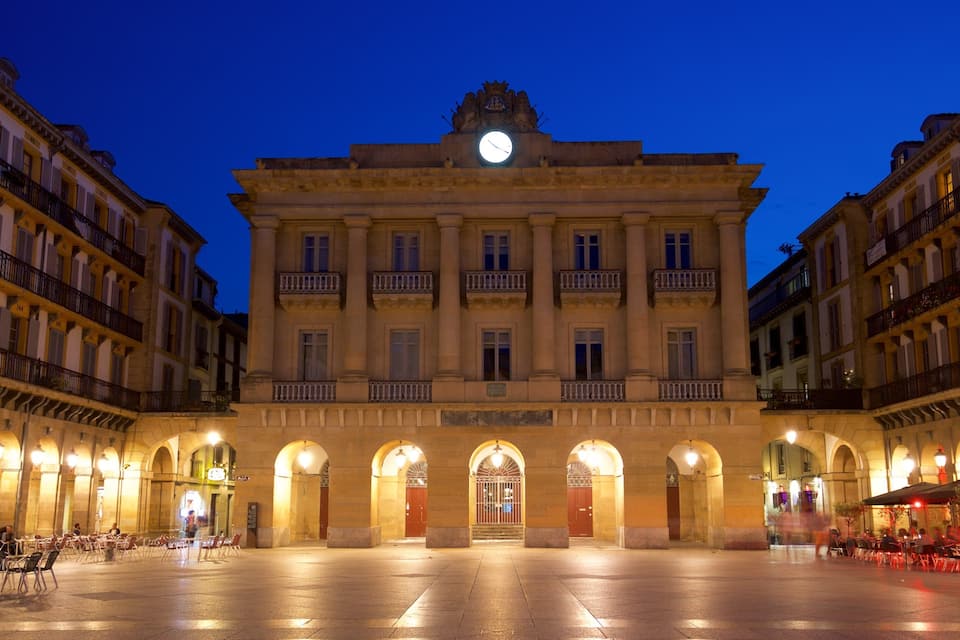 A historic building with a clock tower, arched entrances, and surrounding cafes.