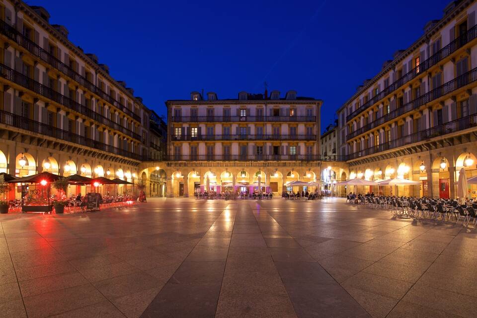 A square with cafes and outdoor seating, surrounded by historic buildings with balconies and arched windows.