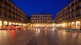 Una plaça amb cafeteries i terrasses, envoltada d'edificis històrics amb balcons i finestres d'arc.
