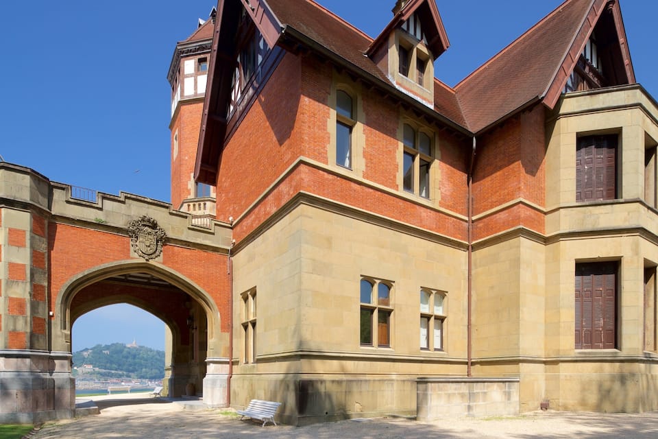 A historic building with a prominent archway, a clock tower, and a view of the sea.