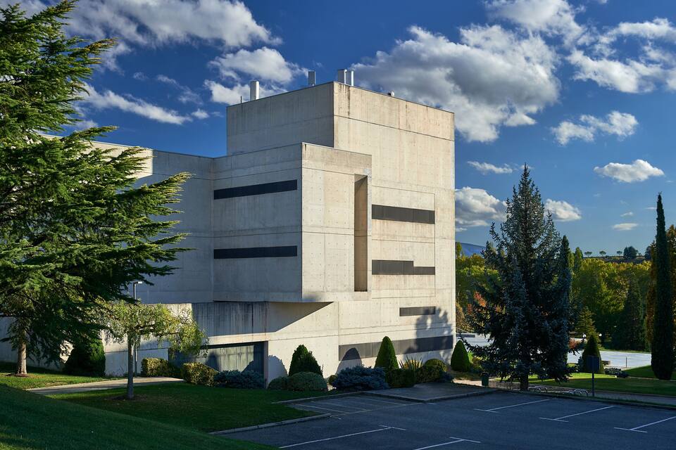 Un edificio moderno con facciata in cemento, circondato da un prato curato e alberi.