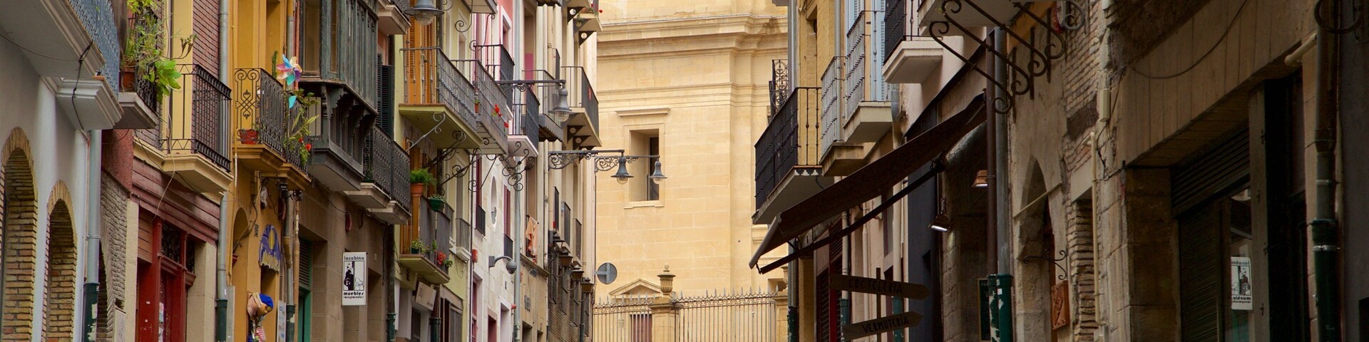 Uma rua estreita com edifícios coloridos, uma torre do relógio e pessoas caminhando.