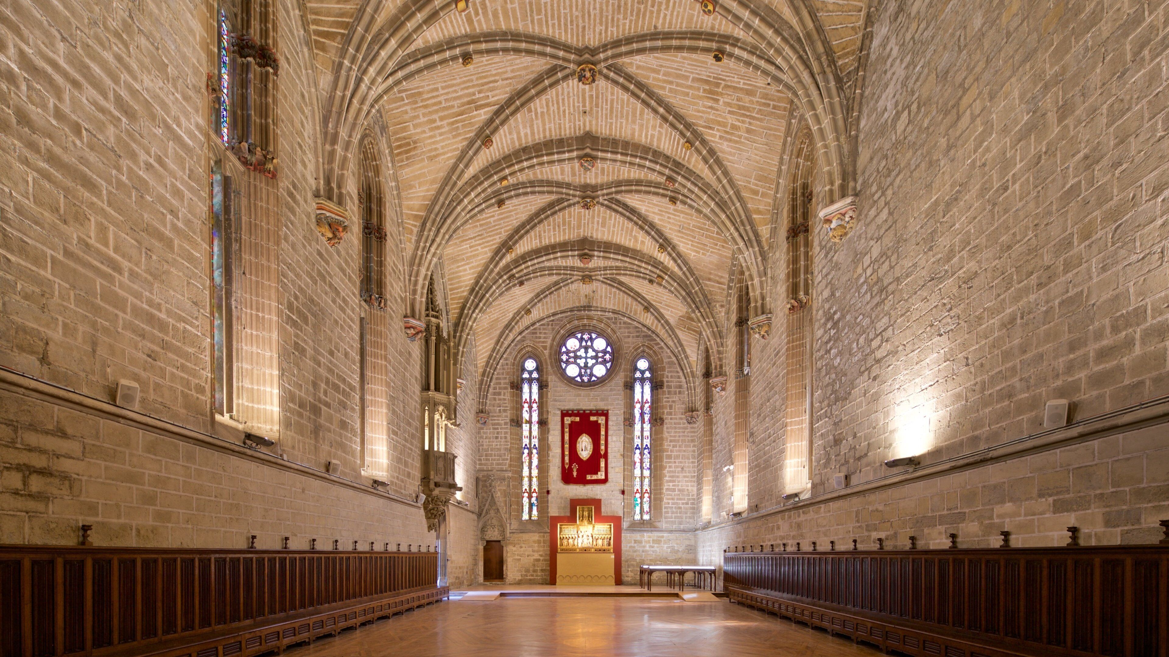 Interior de una catedral con altas bóvedas, vidrieras y bancadas de madera.