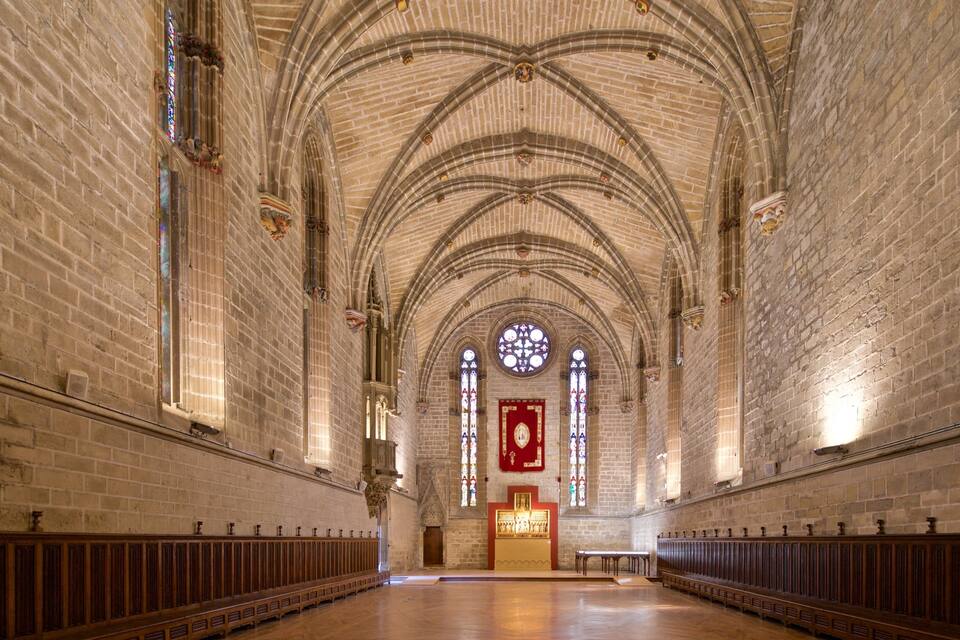 Interior de una catedral con altas bóvedas, vidrieras y bancadas de madera.