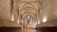 A cathedral interior with high vaulted ceilings, stained glass windows, and a wooden pews arrangement.