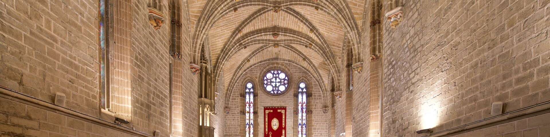 Interior de uma catedral com altos tetos abobadados, janelas de vitrais e disposição de bancos de madeira.