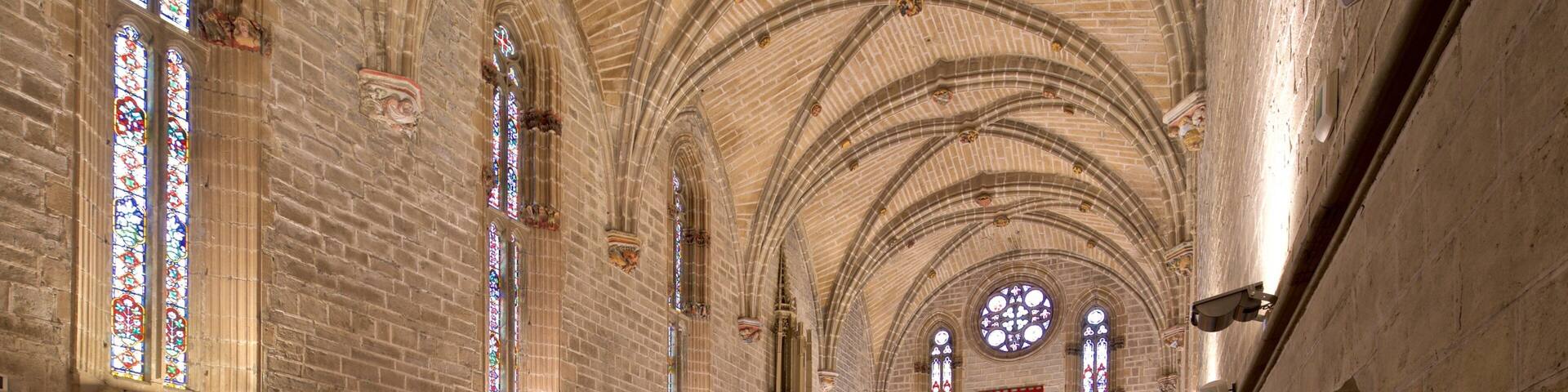 Interior de una catedral con altos techos abovedados, vidrieras de colores y bancas de madera.