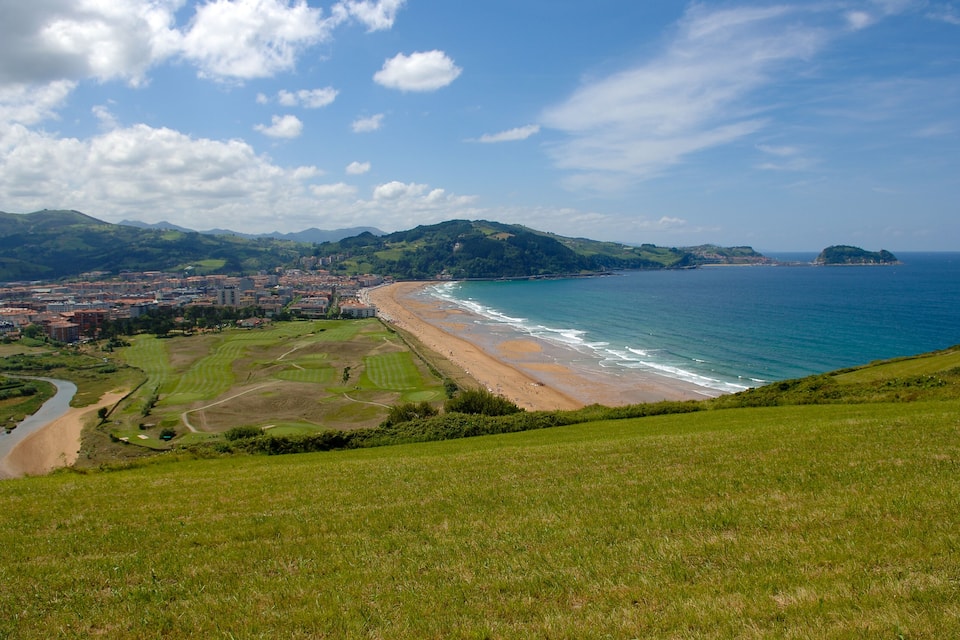 A coastal city with a beach, green hills, and a river.