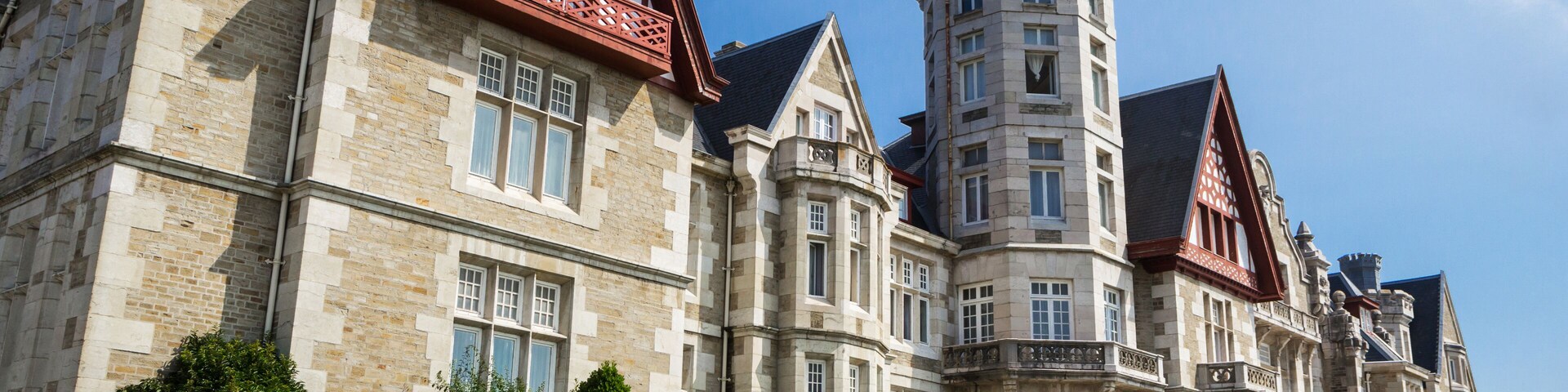 Un edificio grande e histórico con una torre, fachada de piedra y detalles en rojo.