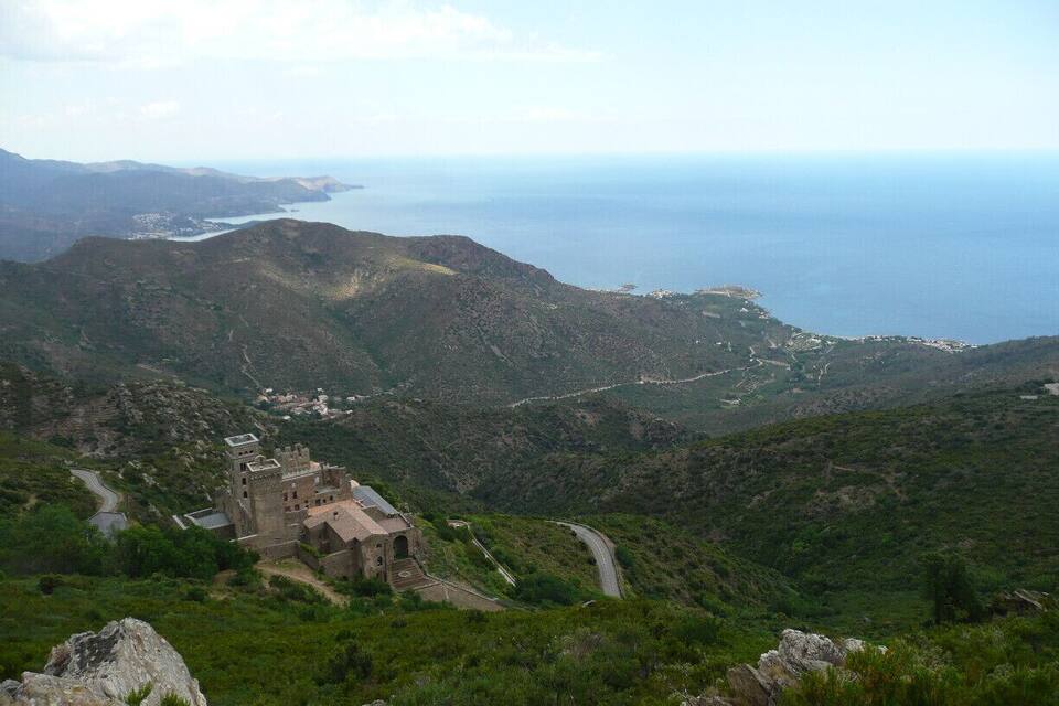 A mountainous landscape with a castle-like structure surrounded by greenery and a winding road.
