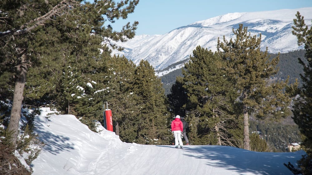 Ein Skifahrer auf einem verschneiten Hang, im Hintergrund schneebedeckte Berge.