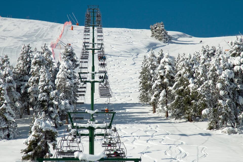 Una seggiovia tra alberi innevati e un cielo azzurro limpido.