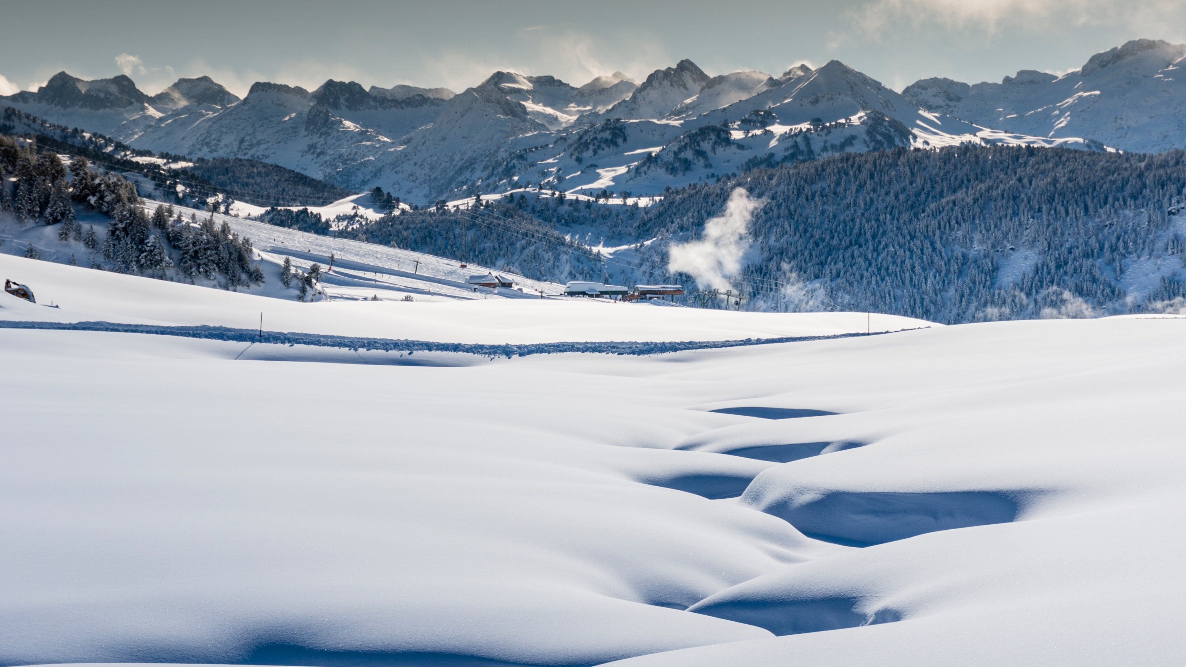 A snow-covered valley with mountains in the background and a ski lift visible.