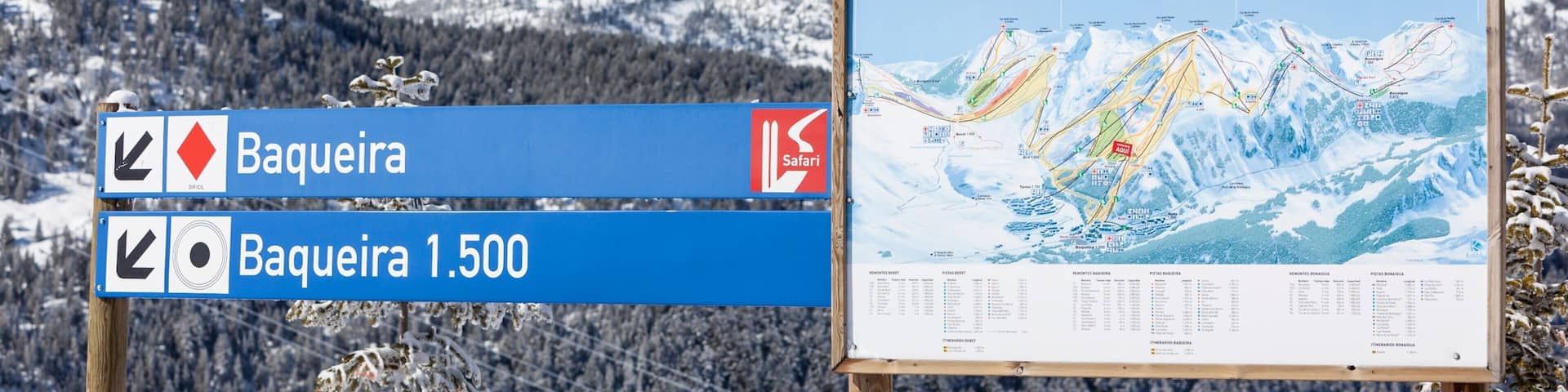A signpost with directions to Baqueira and Baqueira 1.500, a map of ski trails, and a snowy mountainous landscape.