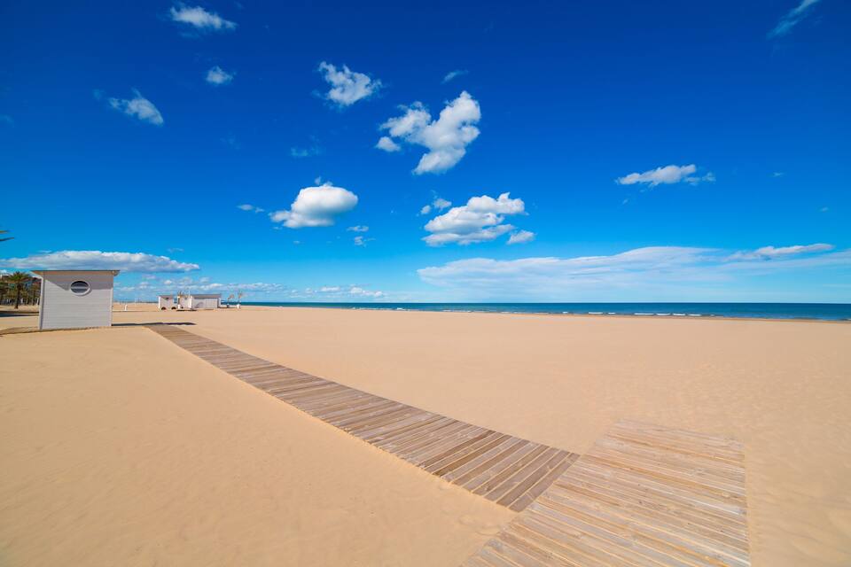 A beach with a wooden boardwalk leading to a small white building.