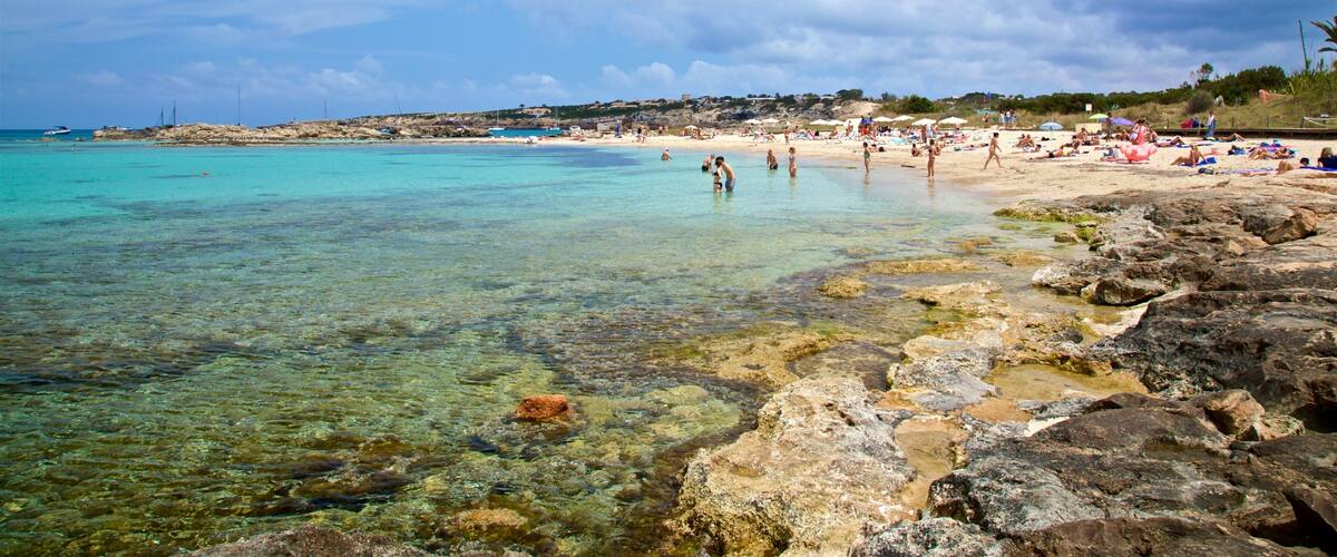 A beach with clear turquoise water, rocky shoreline, and people sunbathing.