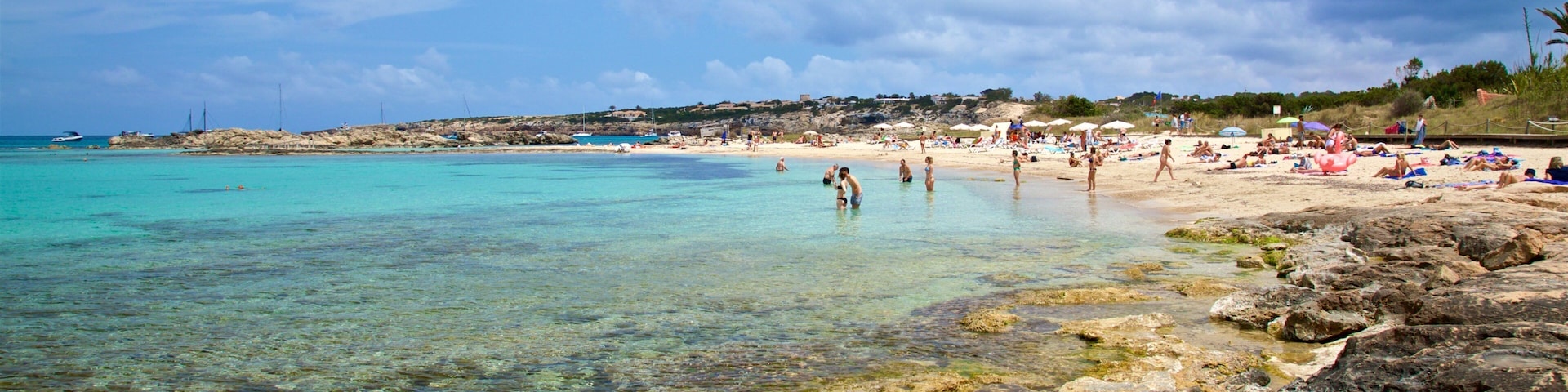 A beach with clear turquoise water, rocky shoreline, and people sunbathing.
