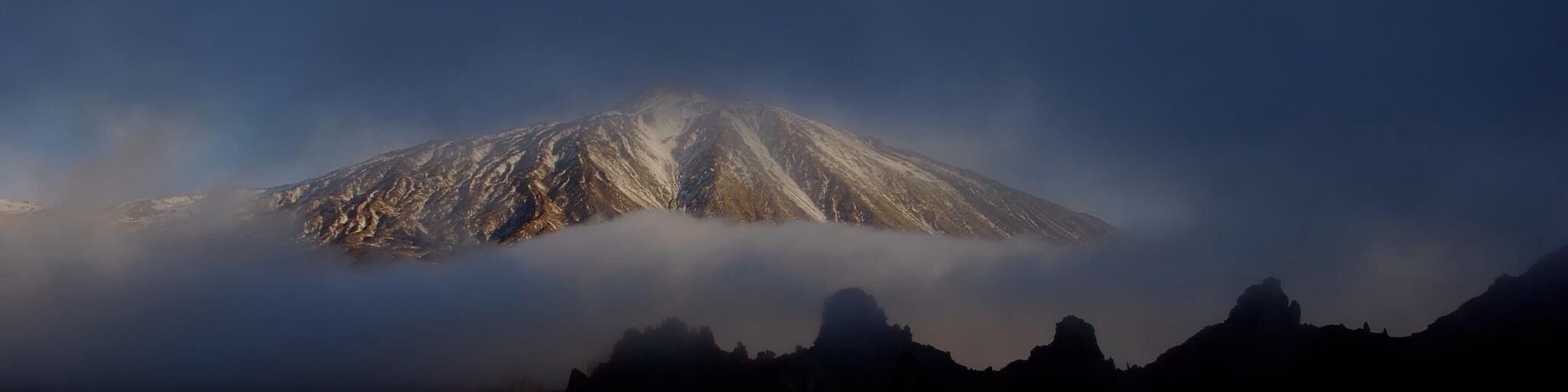 Ein von Wolken teilweise verdeckter, schneebedeckter Berg.