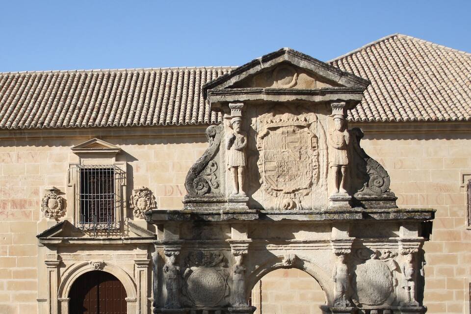 Un edificio histórico con tejado de tejas, un arco de piedra ornamentado y un escudo de armas.
