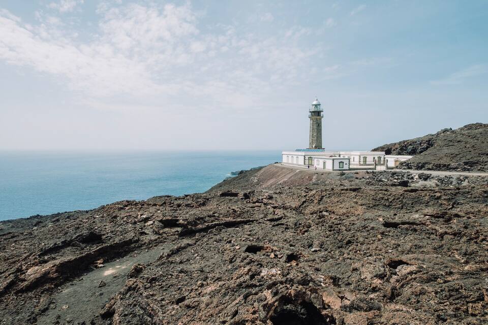 Ein Leuchtturm an einer felsigen Küste, im Hintergrund das Meer.
