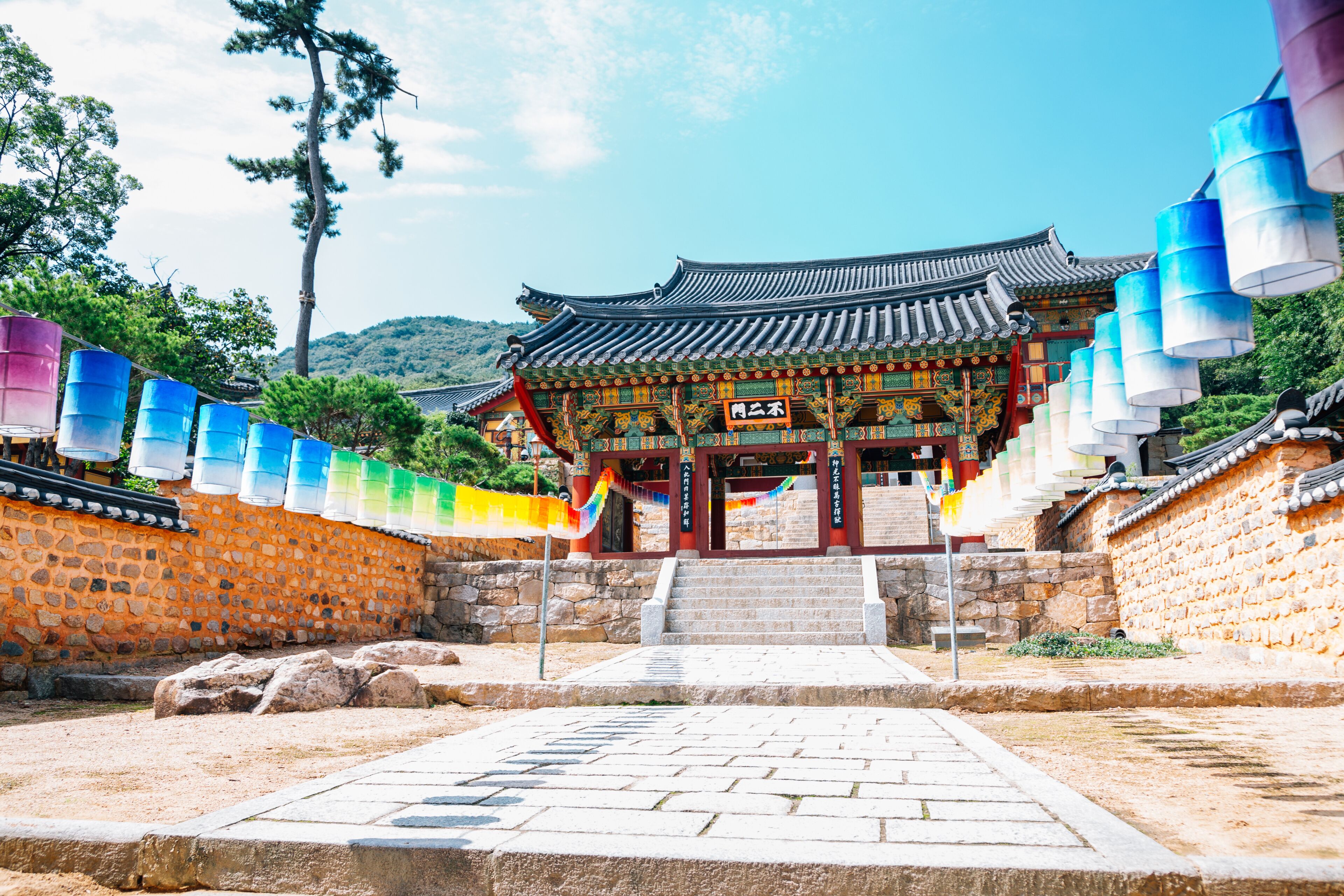 A traditional Korean gate with colorful lanterns, stone walls, and a mountainous backdrop.