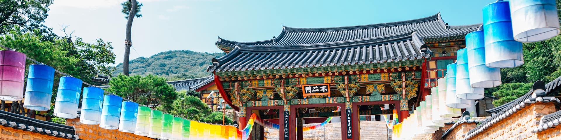 A traditional Korean gate with colorful lanterns, stone walls, and a mountainous backdrop.