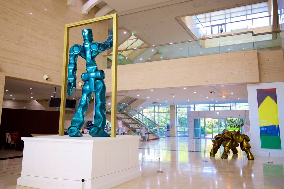 A modern building interior with a large turquoise sculpture, glass railings, and a golden sculpture.