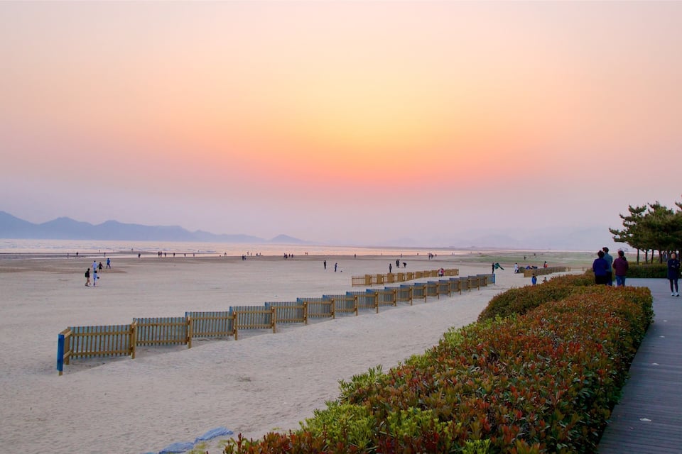 A beach with a wooden fence and a boardwalk with people walking.