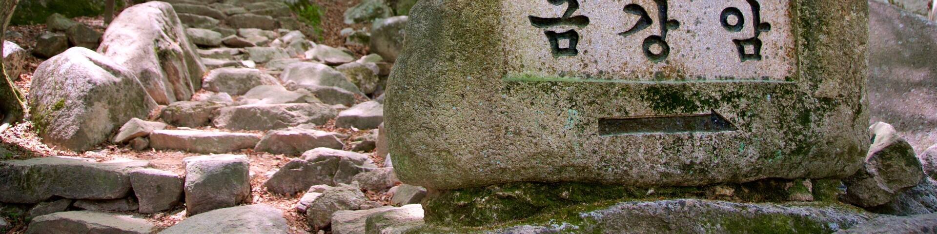 A stone sign with Korean text in a forested area with a rocky path.