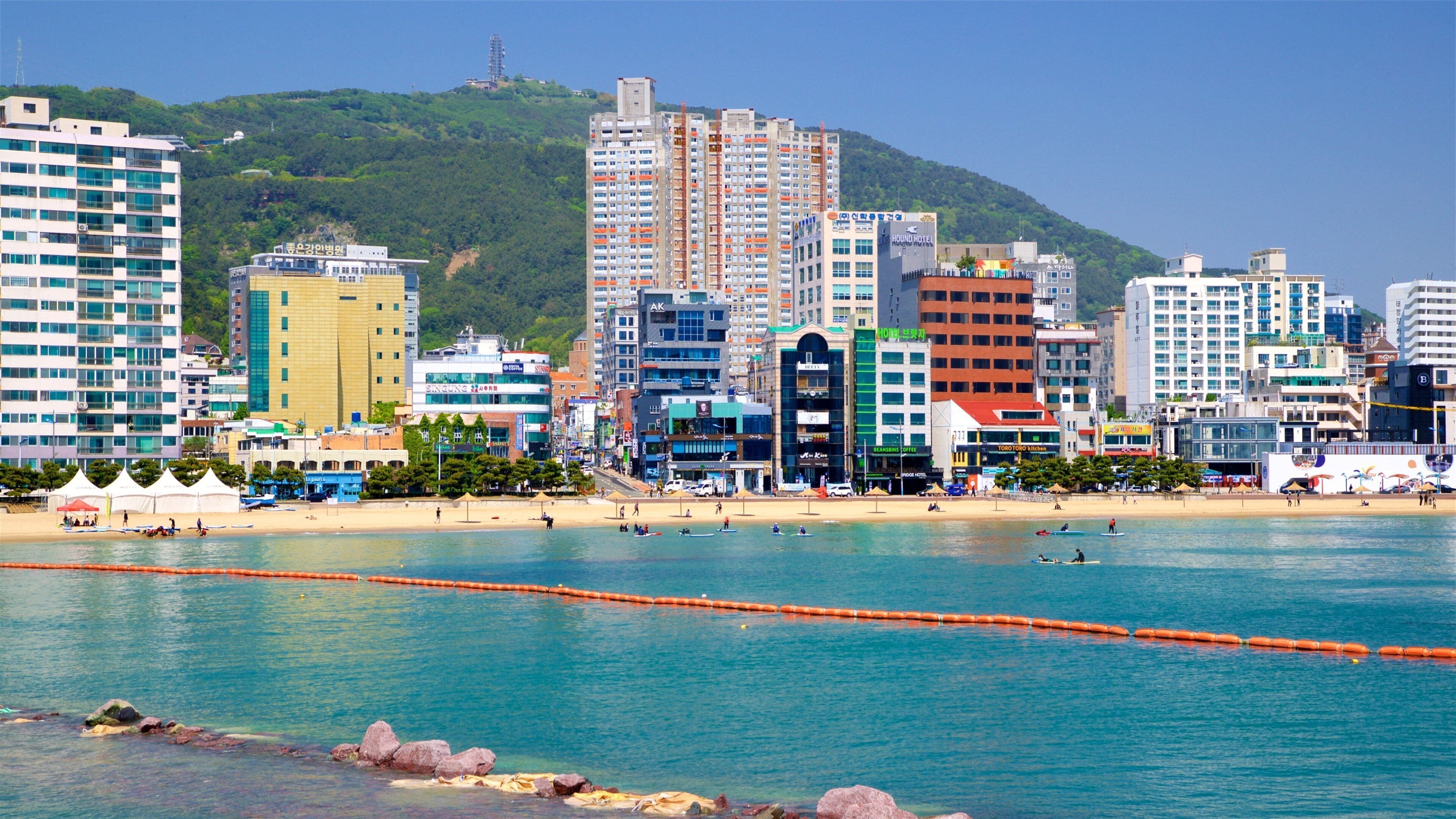 Un paysage urbain côtier avec une plage, des bâtiments et une colline en arrière-plan.