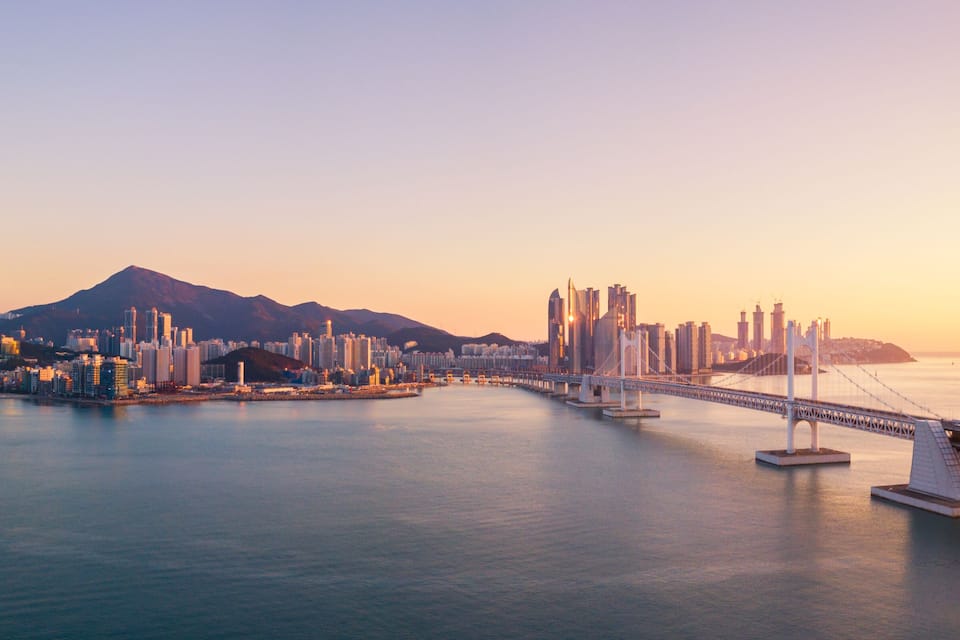 A coastal cityscape with a prominent bridge and a mountain in the background.