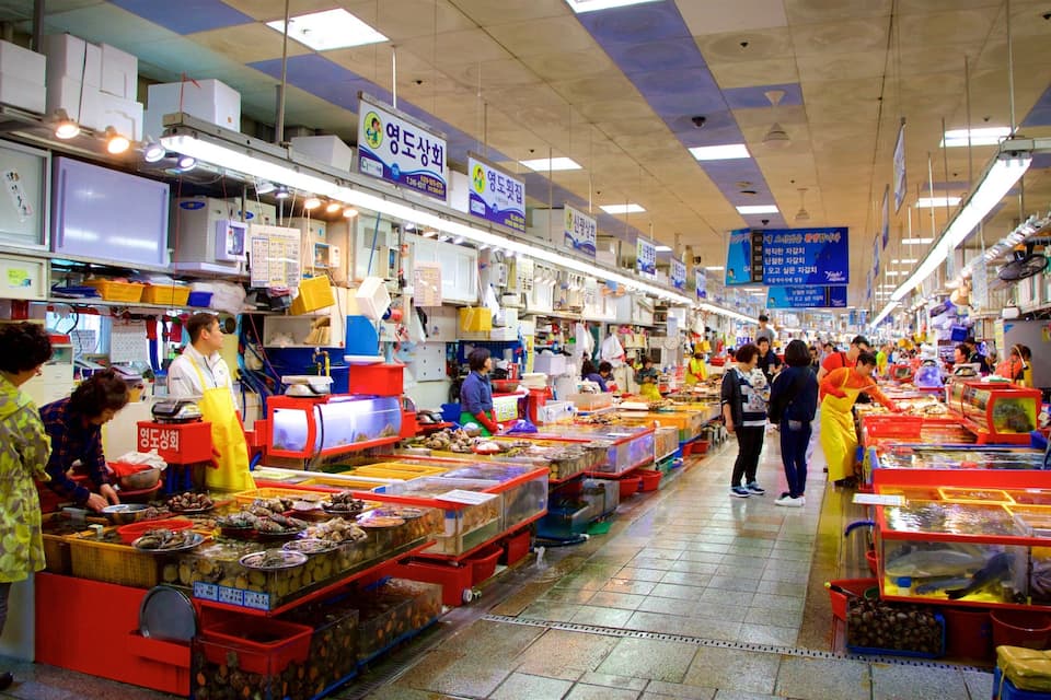 A bustling indoor market with various stalls selling seafood and other goods.