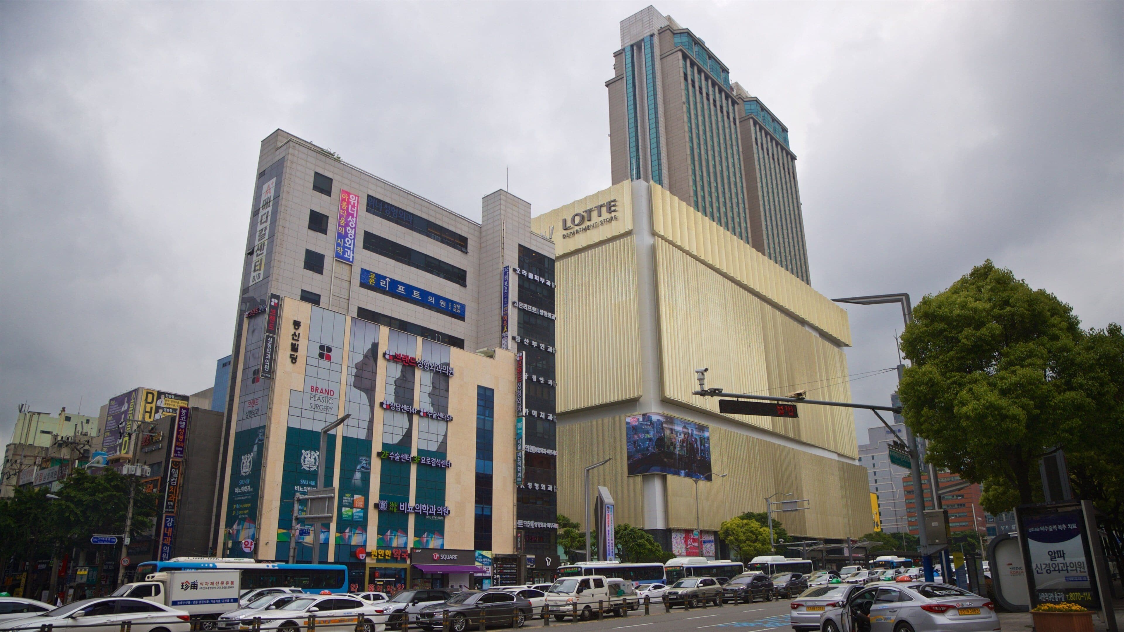 A busy urban street with tall buildings, including a department store and a plastic surgery clinic.