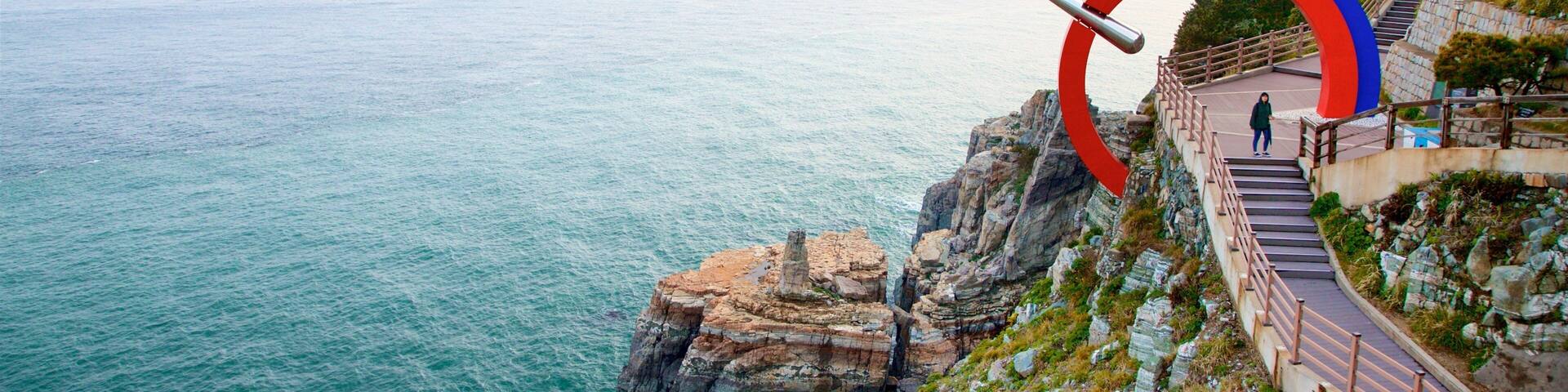 A coastal cliff with a metal sculpture, a staircase, and a view of the sea.
