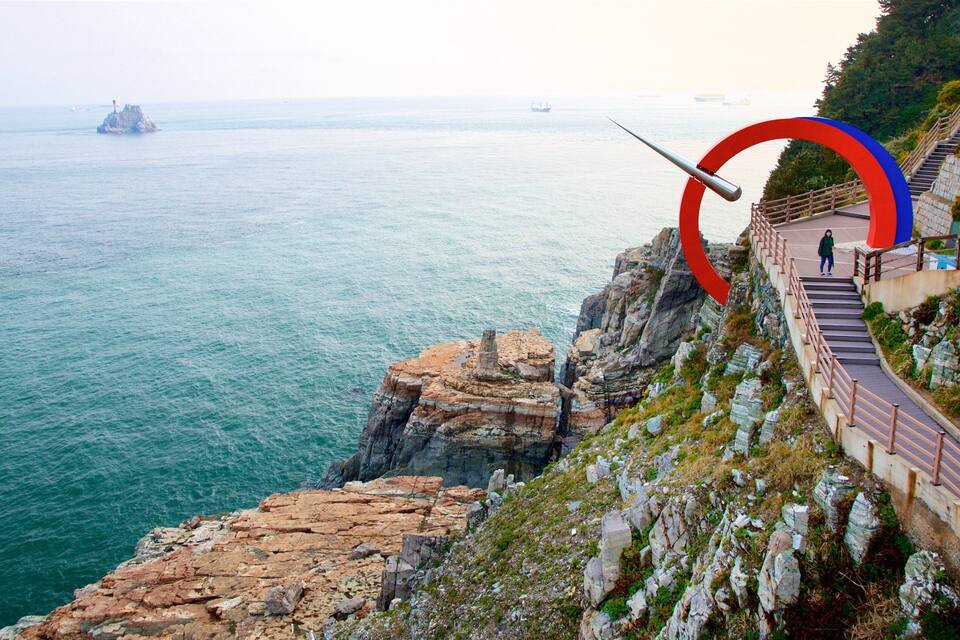 A coastal cliff with a metal sculpture, a staircase, and a view of the sea.